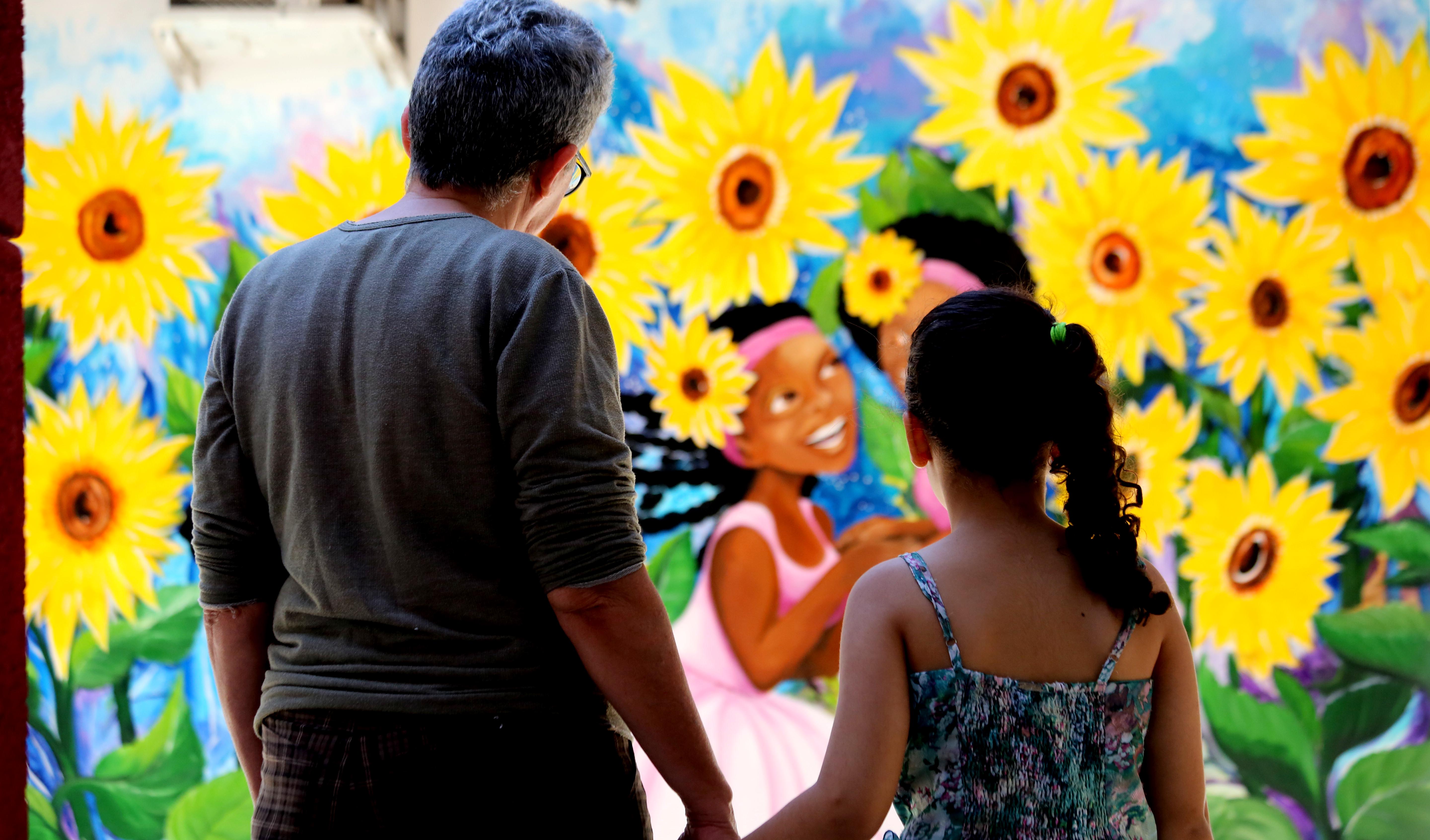 uma mulher e uma criança de costas olham para um mural com flores 